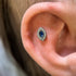 Close-up of an ear with a Celeste Eye piercing featuring a blue gemstone.