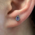 Close-up of an ear wearing a teardrop-shaped piercing with a purple gemstone.